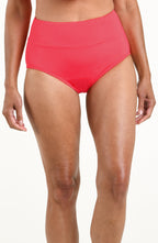 Woman wearing a solid bright orange mid waist bottom against a white background. 