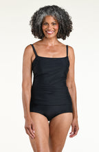 Woman wearing a solid black one piece swimsuit against a white background. 