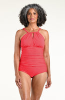 A woman modeling a coral red halter-neck one-piece swimsuit against a plain white studio background.