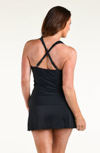 A woman modeling a black halter-neck tankini top and matching swim skirt against a plain white studio background.