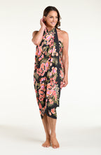 A woman modeling a black wrap sarong with a vibrant pink, orange, and green floral print, featuring a high side slit and a tied waist.