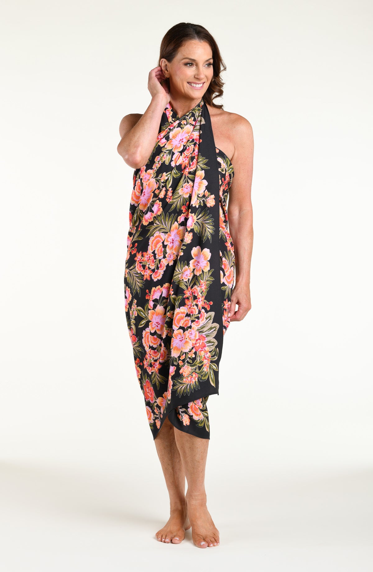 A woman modeling a black wrap sarong with a vibrant pink, orange, and green floral print, featuring a high side slit and a tied waist.