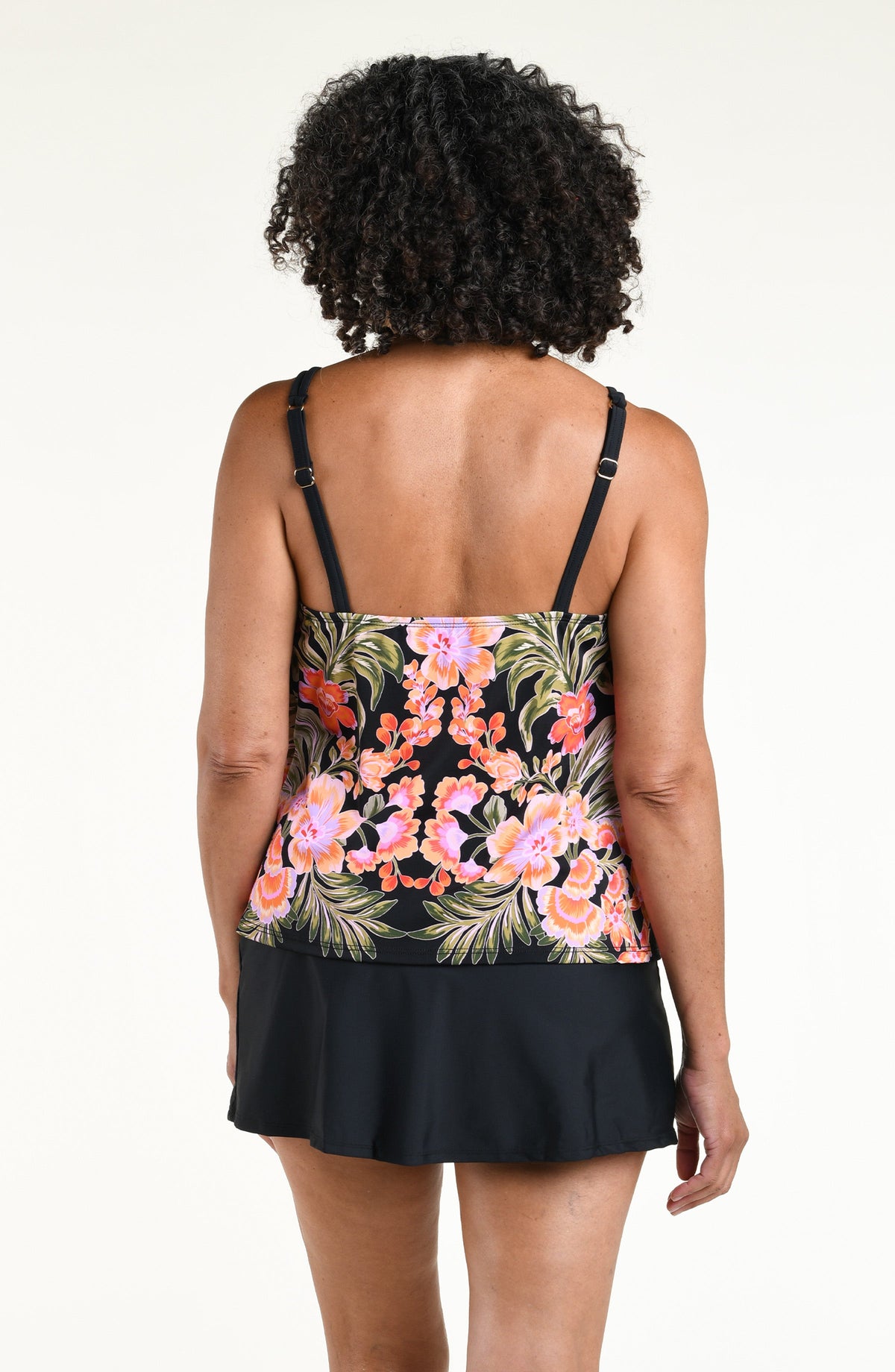 Woman wearing a black multicolored tankini top and solid black swim skirt against a white background. 