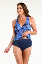 Woman wearing an indigo blue multicolored tankini top and solid indigo blue bikini bottoms against a white background. 