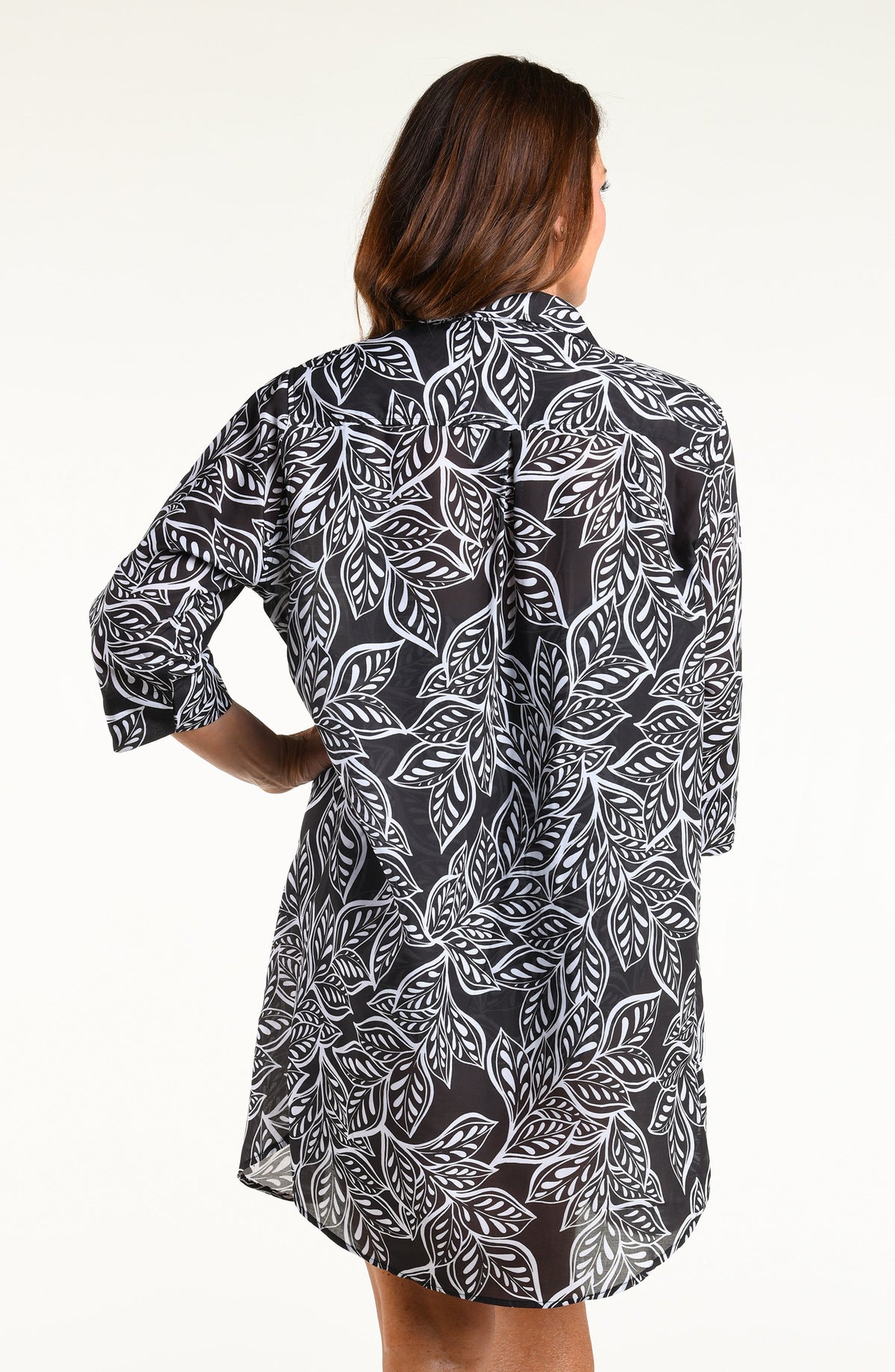 A woman modeling a black and white tropical leaf print tunic with three-quarter sleeves and a high-low hem, shown against a plain white studio background.