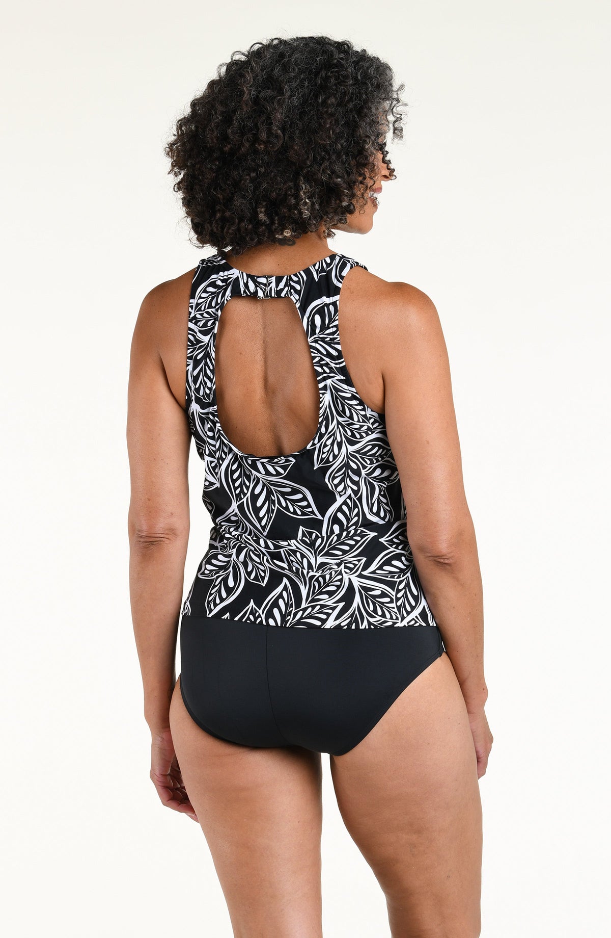 Woman wearing a black and white multicolored tankini top with a solid black bottom against a white background. 