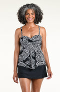 A woman wearing a black and white tropical leaf print camisole top and a black swim skirt, standing against a plain off-white studio background.