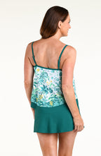 A woman modeling a tankini top featuring a tropical floral print and a solid teal swim skirt, set against a plain white studio background.