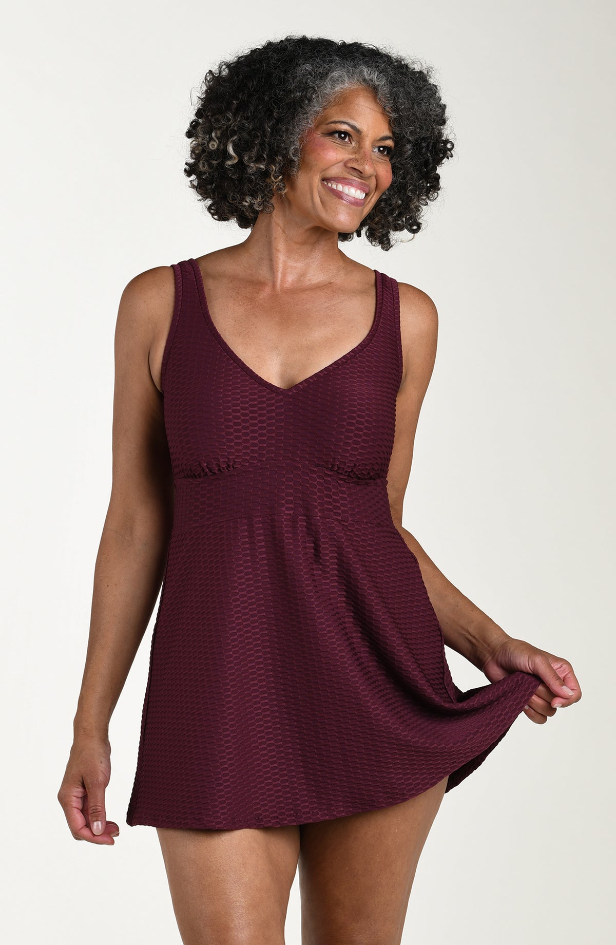Front image of model wearing a solid wine colored one piece swim dress featuring a v-neckline, fixed shoulder straps, and full coverage. 