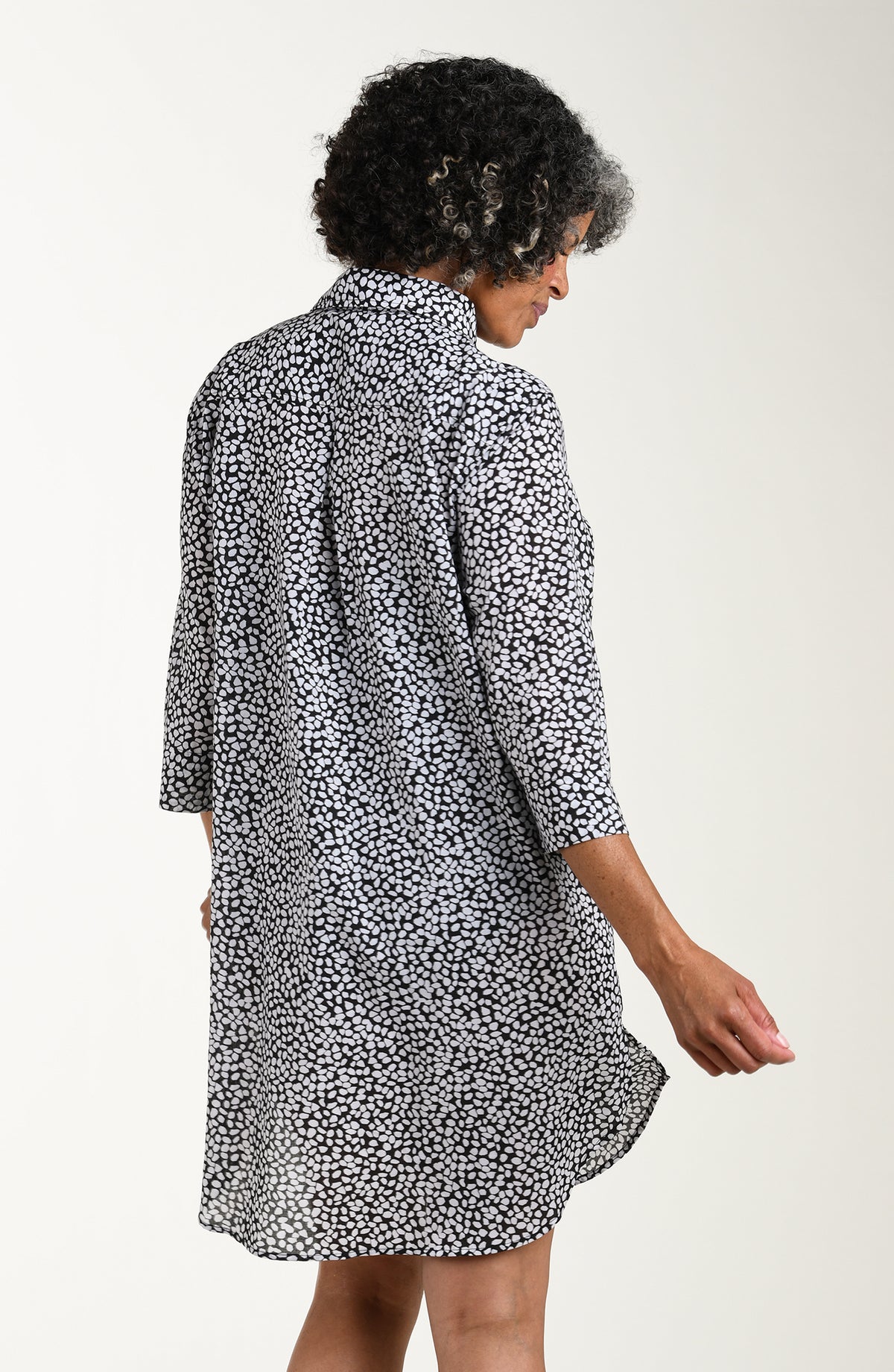 Woman wearing a black and white patterned cover up shirt over a black swimsuit on a white background
