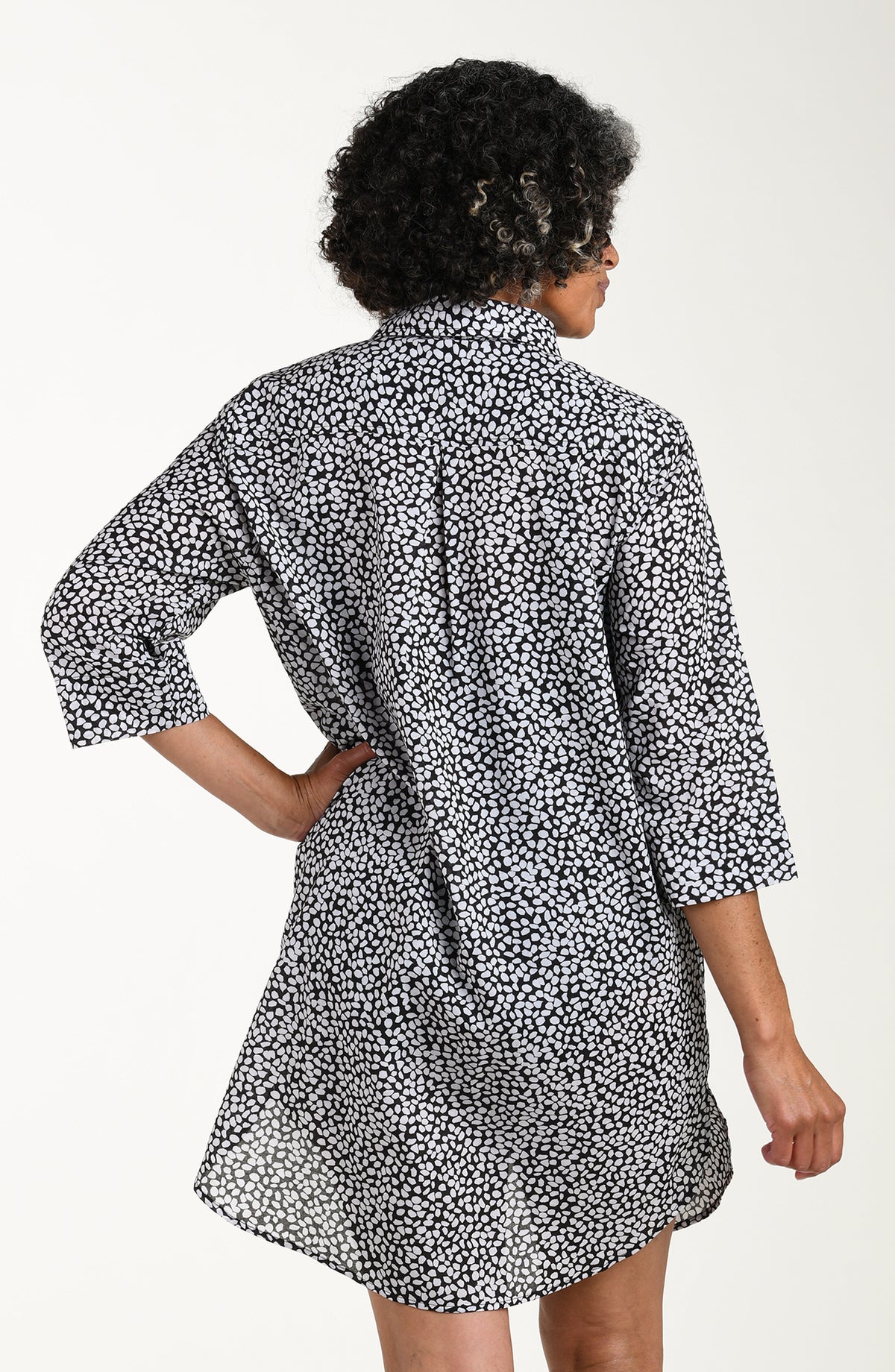Woman wearing a black and white patterned cover up shirt over a black swimsuit on a white background
