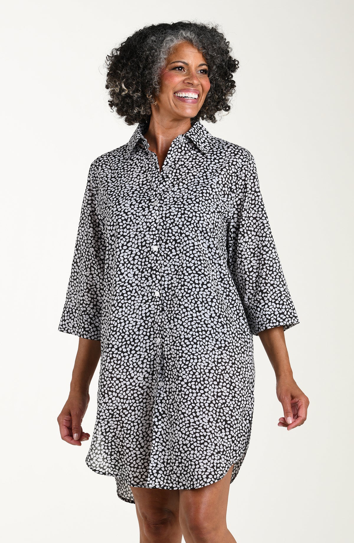 Woman wearing a black and white patterned cover up shirt over a black swimsuit on a white background