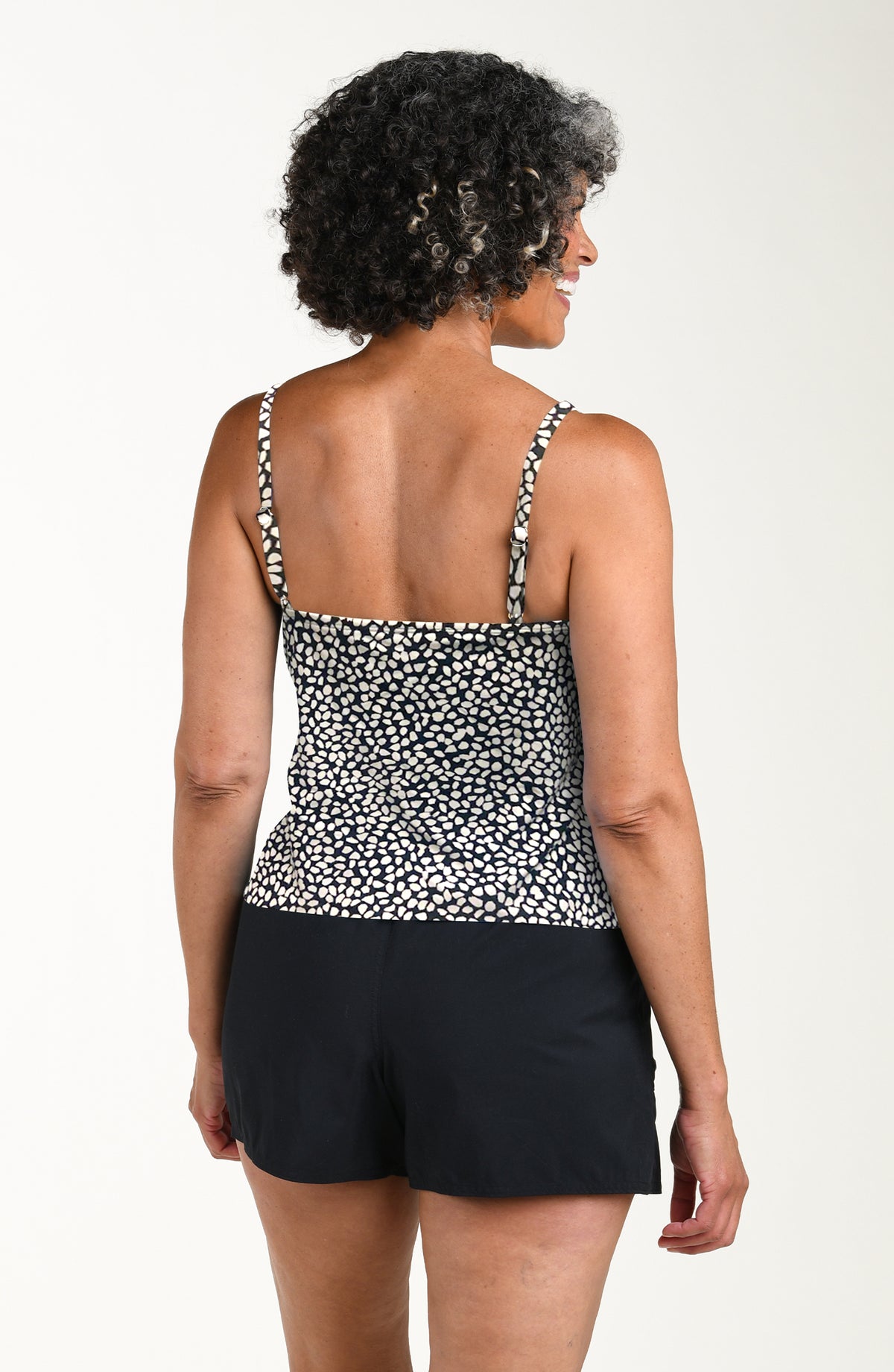 Woman wearing a black and white patterned tankini top and black shorts on a white background