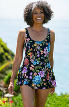 Woman wearing a floral swim dress standing outdoors with a clear blue sky and greenery in the background
