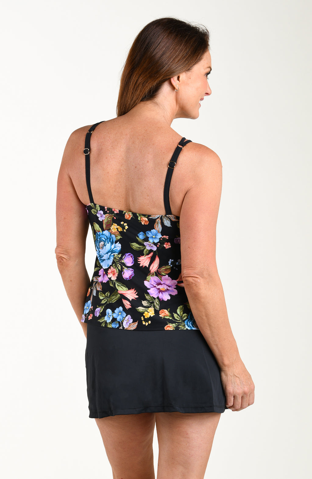 Woman wearing a floral tankini top with a black swim skirt against a plain background
