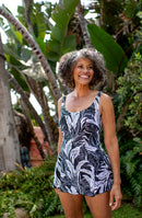 Woman wearing a black and white leaf-patterned swim dress standing in a tropical setting with greenery.