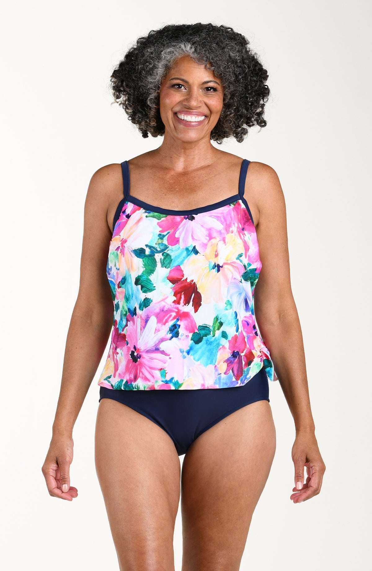 Woman wearing a colorful floral tankini and indigo bottoms set on a plain background
