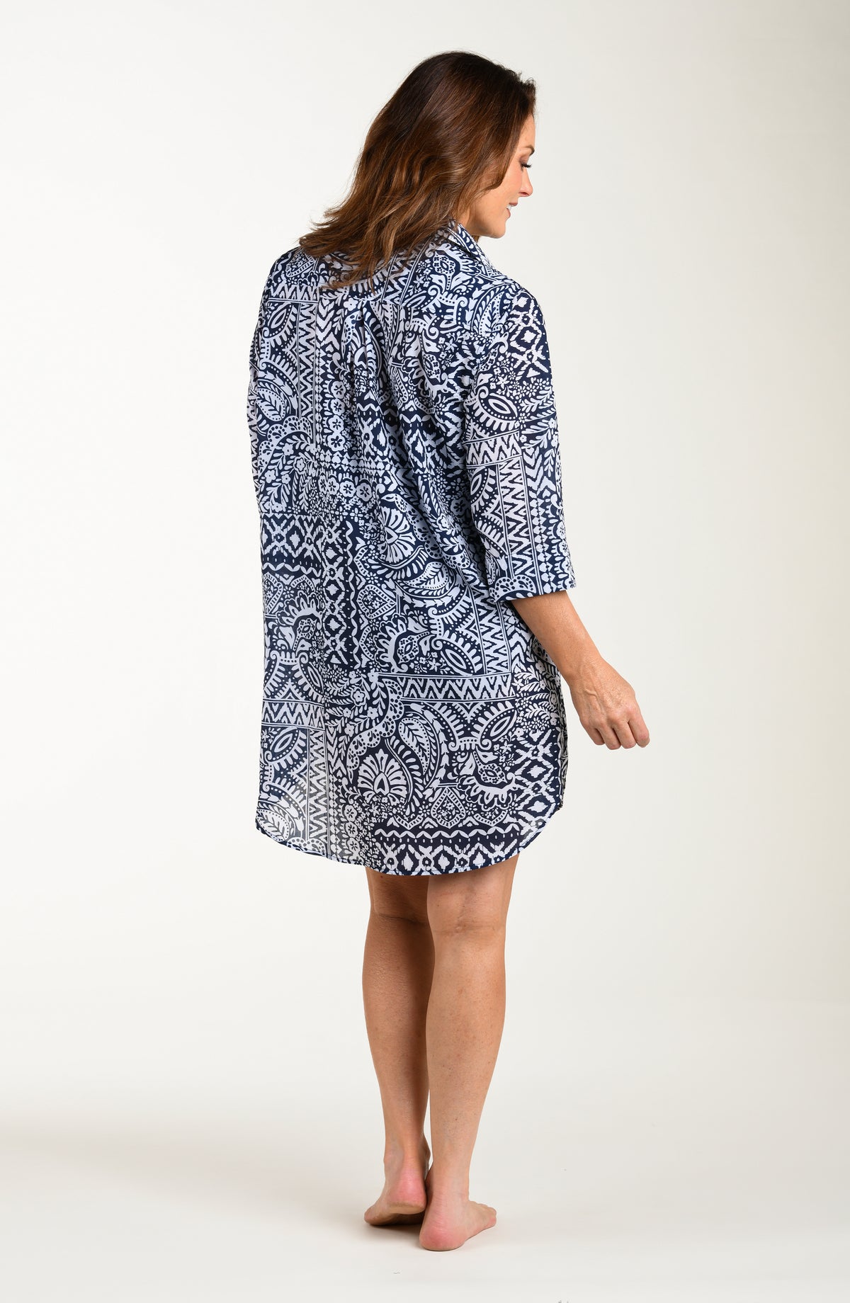 Full body back image of model wearing a multicolored navy blue paisley printed tunic cover up featuring a collared button front and three quarter sleeves. 