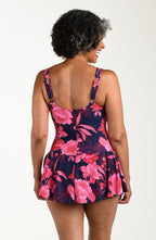 Back image of model wearing a multicolored (pink) floral printed one-piece swim dress with wide straps, a scoop neckline, flared skirt, and full rear coverage.