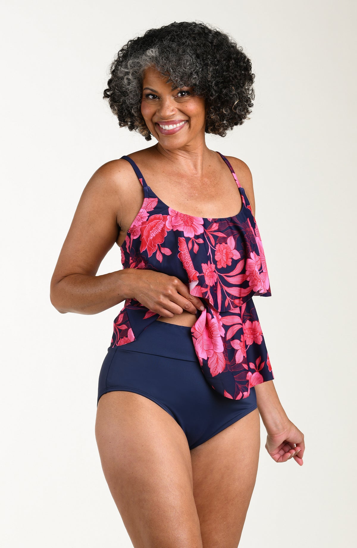 Front image of model wearing a multicolored (pink) floral printed tankini featuring thin over the shoulder straps and two tiers of ruffled layers.