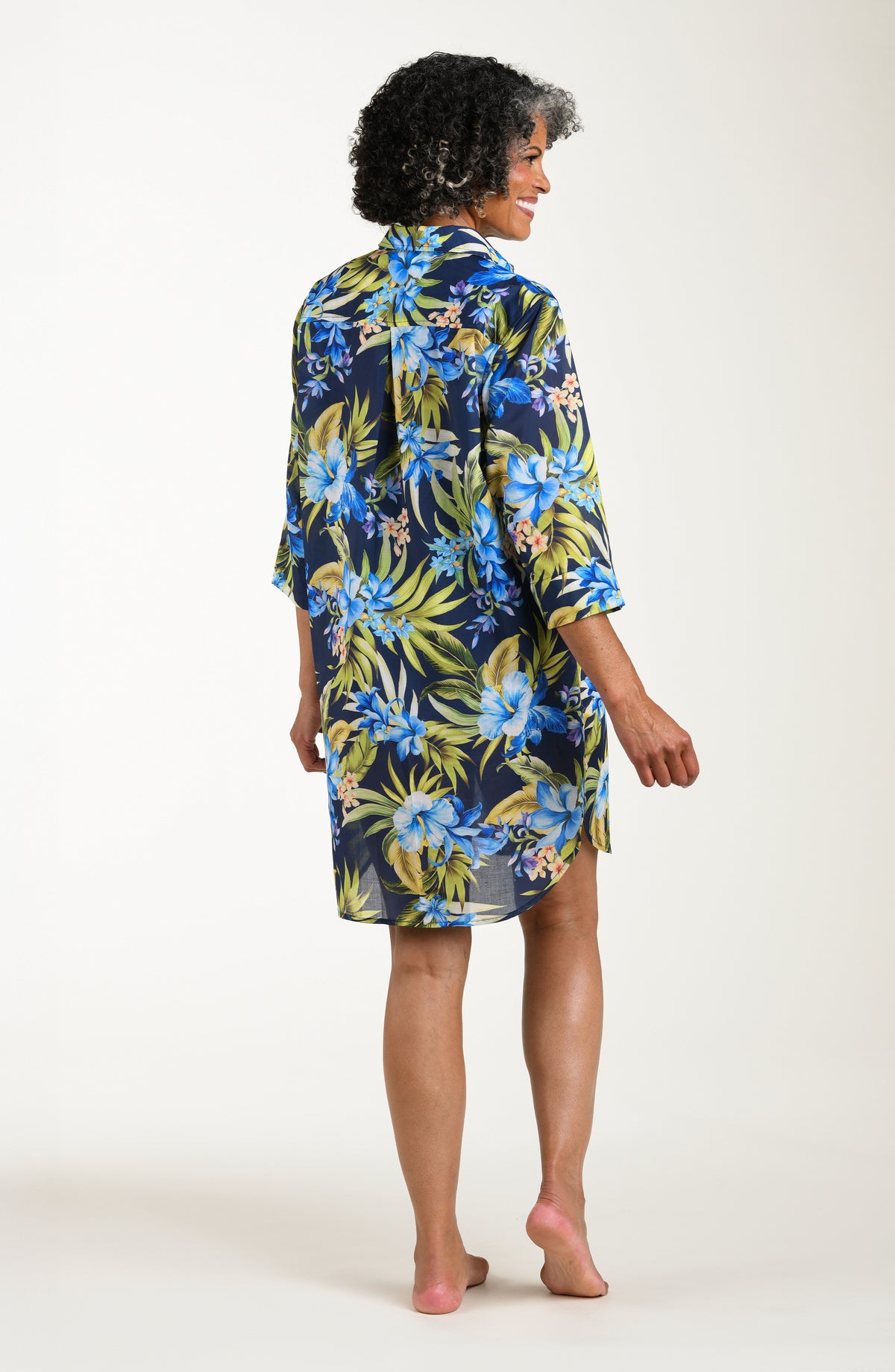 Back image of model wearing a multicolored (blue) tropical tunic cover up featuring a collared button front and three quarter sleeves. 