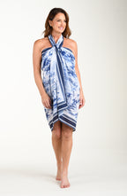 Full body front image of model wearing a multicolored white and blue tropical pareo which is tied at the neckline. 