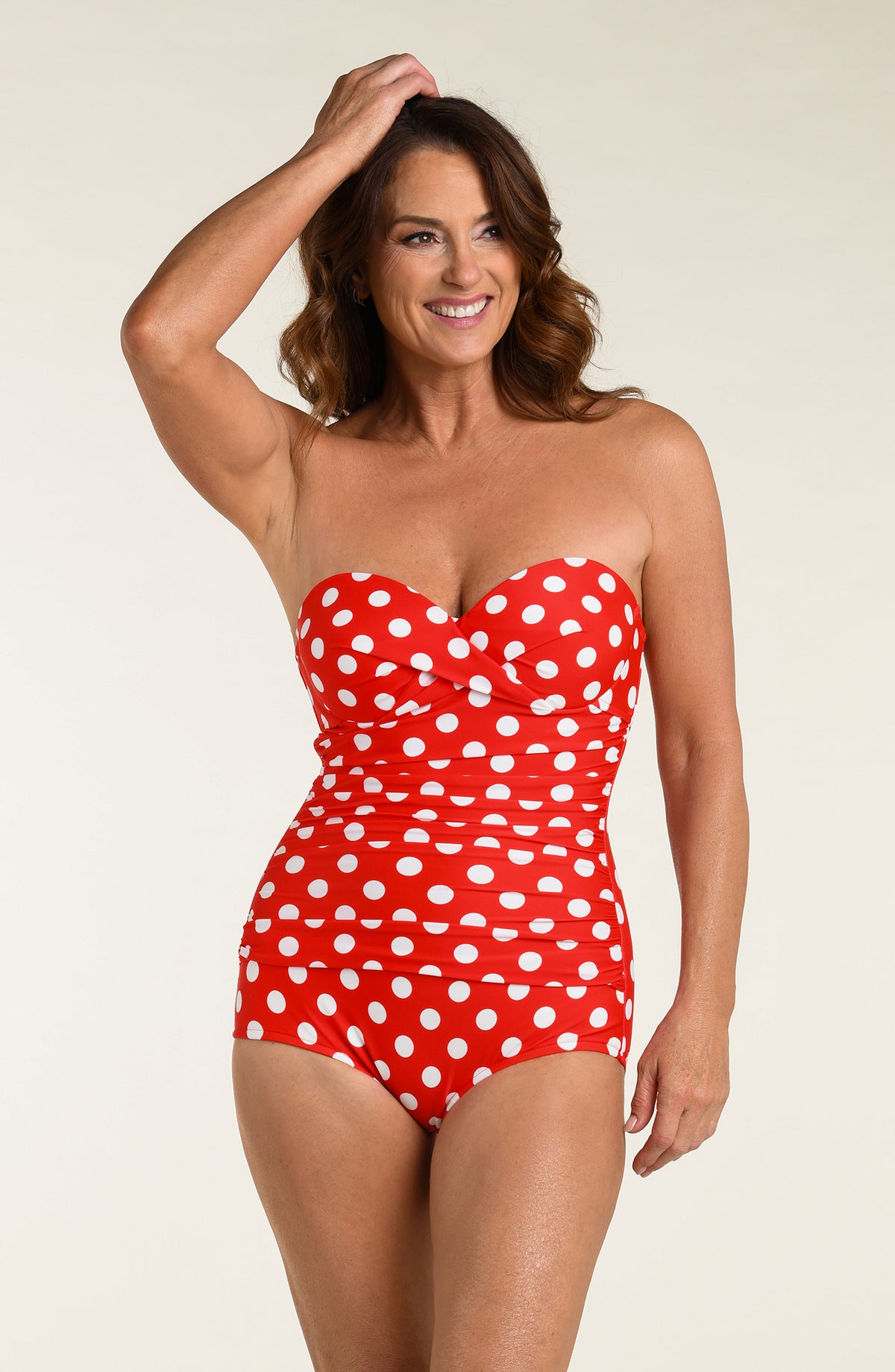 Woman wearing a red polka dot one piece swimsuit on a plain background