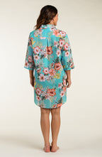 Woman wearing a floral button up cover up shirt against a plain background