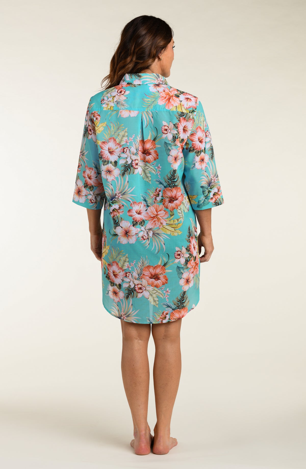 Woman wearing a floral button up cover up shirt against a plain background