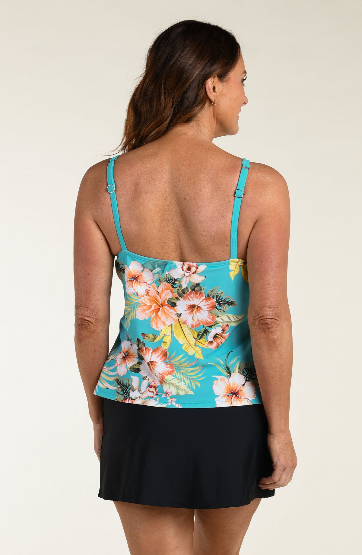 Woman wearing a floral tankini top and black swim skirt with a white background