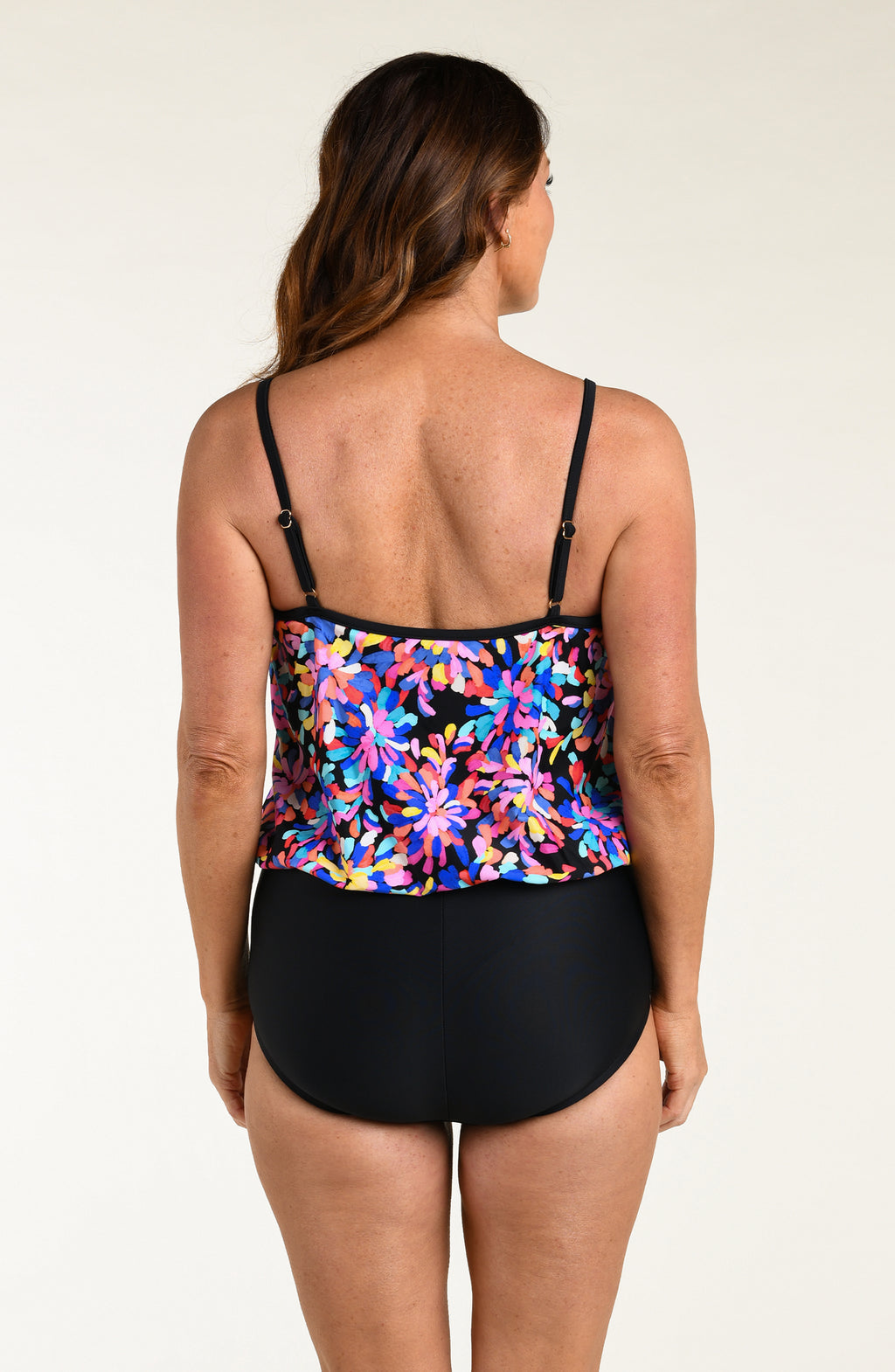 Woman wearing a colorful floral tankini top and black black bottoms on a plain background