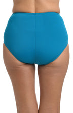 A close-up of a model wearing high-waisted, solid turquoise blue bikini bottoms against a plain white background.