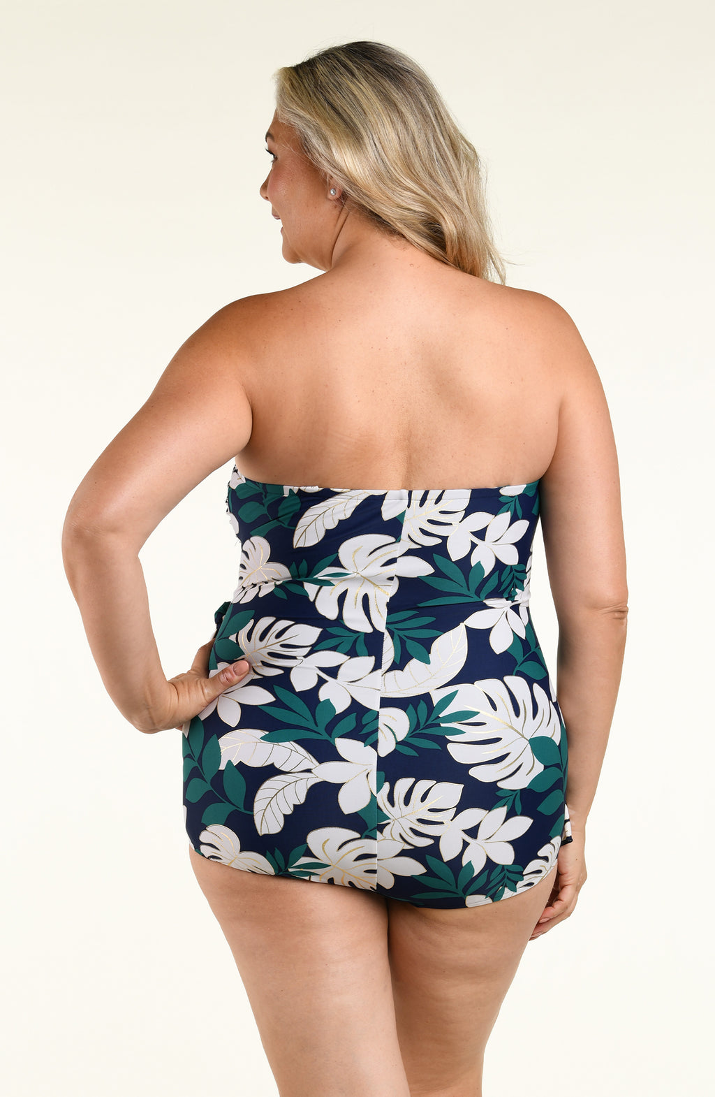 Woman wearing a green multicolored bandeau one piece swimsuit against a white background. 