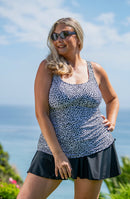 Woman wearing a patterned swim dress and black skirt with sunglasses, standing outdoors against a blue sky.