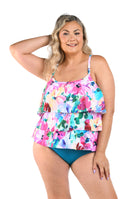 Woman wearing a colorful floral tankini top with emerald bottoms against a white background.