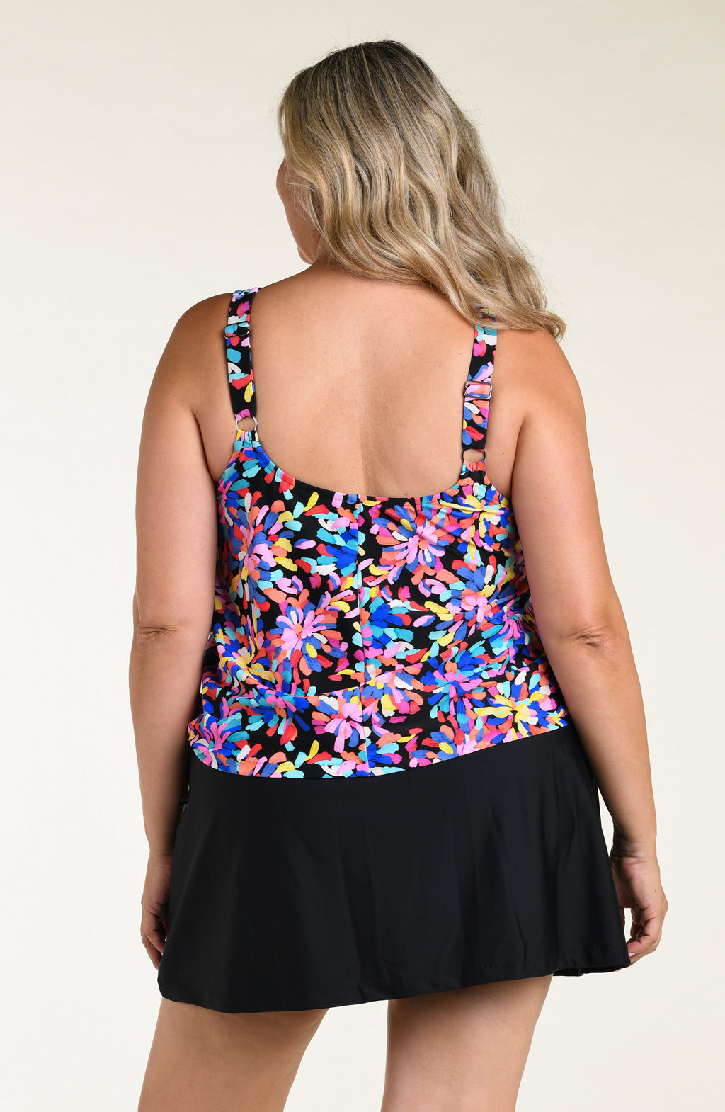 Woman wearing a colorful floral tankini top and black swim skirt bottom against a white background.