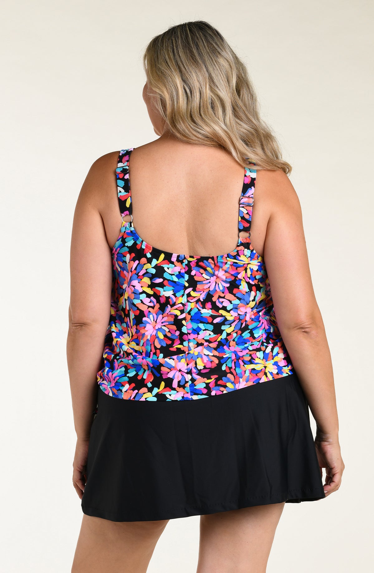 Woman wearing a colorful floral tankini top and black swim skirt bottom against a white background.