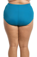 A close-up of a model wearing high-waisted, solid turquoise blue bikini bottoms against a plain white background.