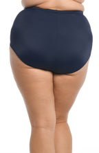 A close-up of a model wearing high-waisted navy blue bikini bottoms against a plain white background.