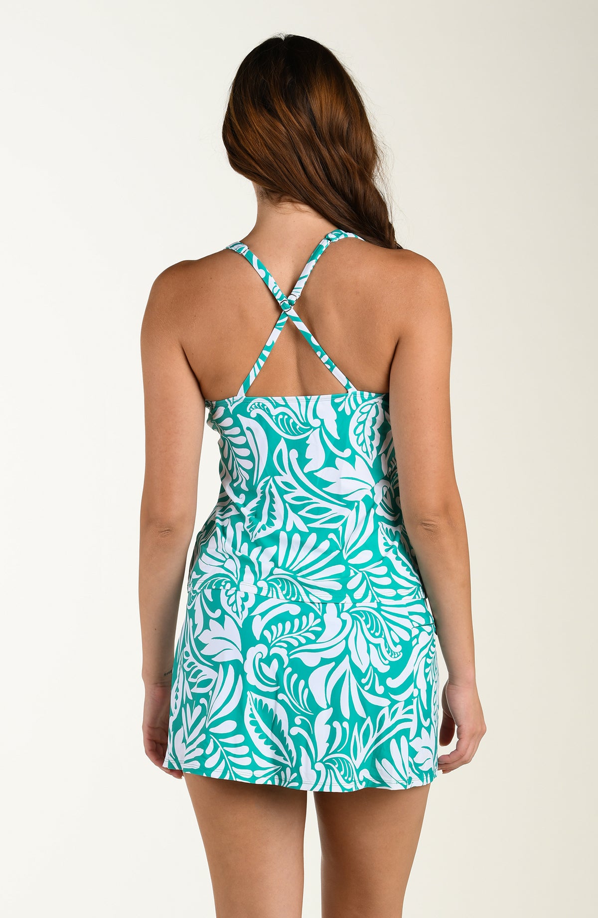 Woman wearing a teal and white patterned tankini top and matching swim bottom on a beige background