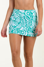 Teal and white tropical patterned swim skirt worn by a person on a beige background