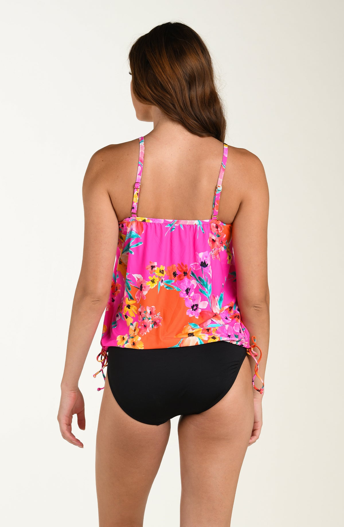 Back image of model wearing a multicolored floral printed tankini top featuring over the shoulder convertible straps, a straight back, and adjustable side ties. This is paired with a solid black bottom. 