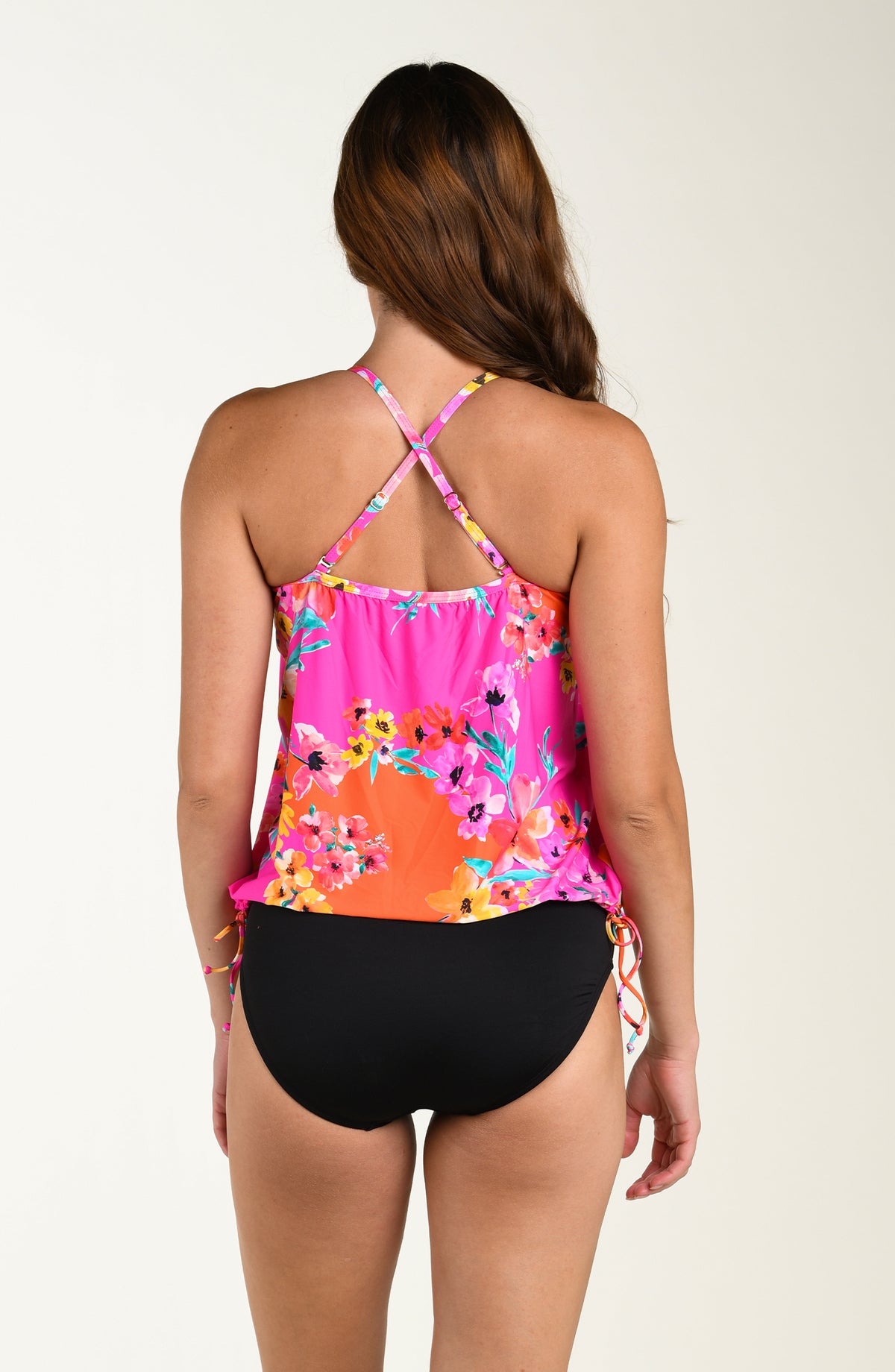 Back image of model wearing a multicolored floral printed tankini top featuring over the shoulder convertible straps, a straight back, and adjustable side ties. This is paired with a solid black bottom. 